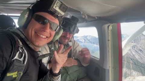 Still from The Airborne Ram — Axel and a partner in a jump plane over the mountains, parachute rigs on